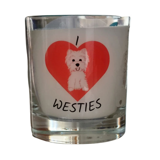 A colourless glass containing white candle wax. On the glass horizontally from the top is I then a large red heart and westies written underneath. In the heart is a picture of a white west highland terrier dog.