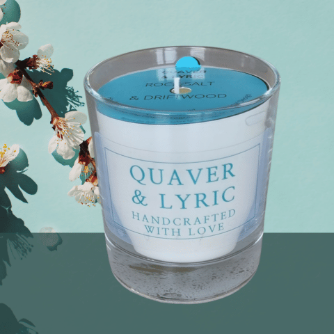 A glass container candle with quaver and lyric label and a blue dust cover