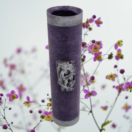 The Quaver&Lyric Wax Vase Tall Cylinder in purple with an aged silver effect makes a striking home decor piece, especially when paired with pink and yellow flowers.