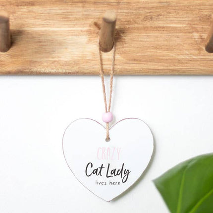 a heart shaped sign which reads crazy cat lady lives here, suspended by a piece of twine and finished with a wooden bead hanging on a wooden coat peg