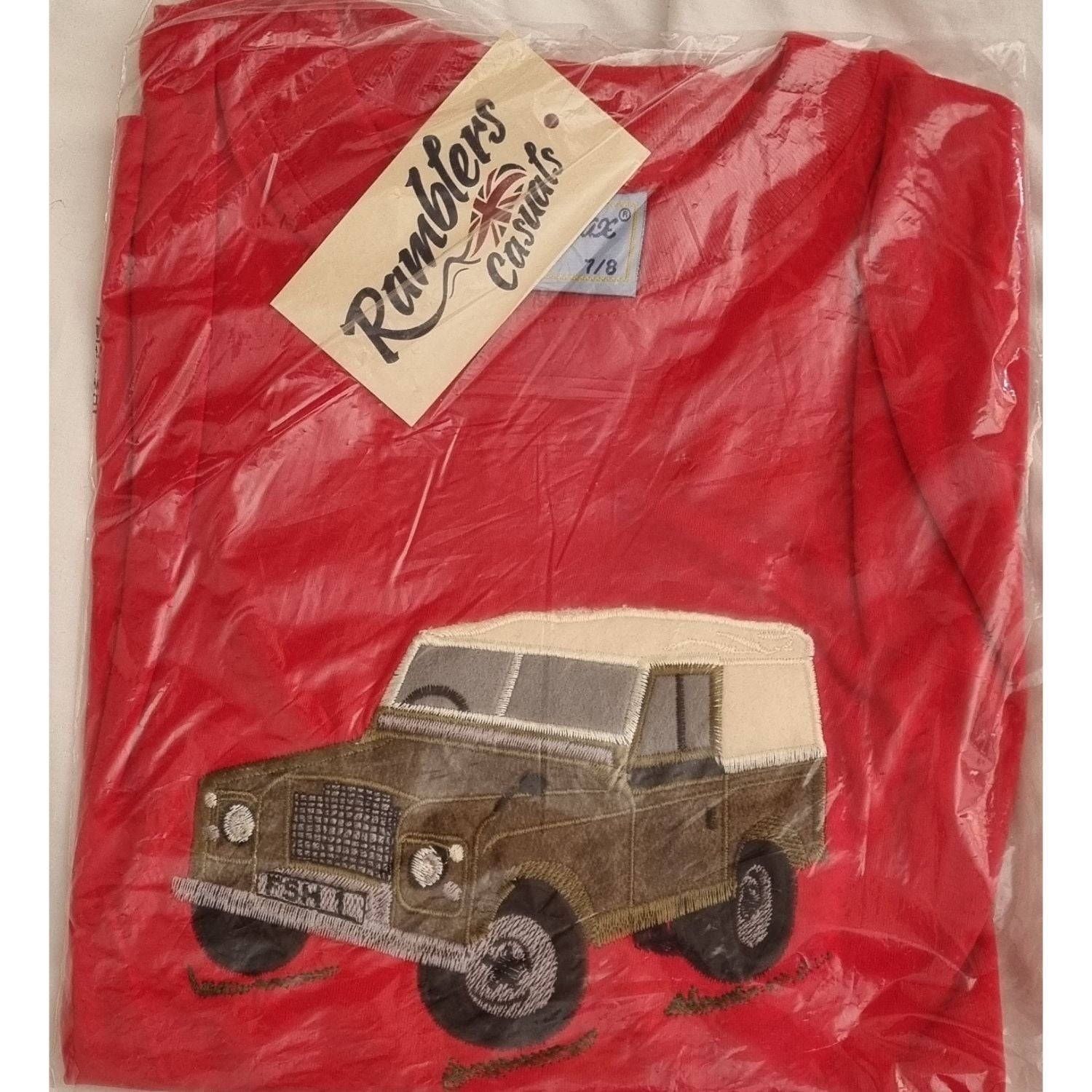 The Ramblers Embroidered T Shirt Farm Vehicle Childrens is a red tee, new in packaging, featuring a green vintage farm vehicleâ€”a perfect addition to any kidâ€™s wardrobe.
