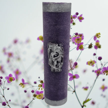 The Quaver&Lyric Wax Vase Tall Cylinder in purple features aged silver effect decoration, standing upright as elegant home decor against a blurred background of pink and yellow flowers.