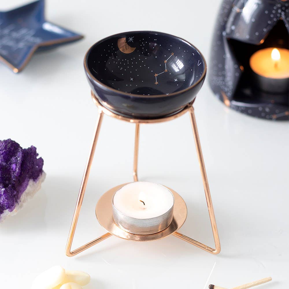 wax warmer with ceramic dish featuring gold celestial accents and a matching gold coloured metal base with lit tealight 