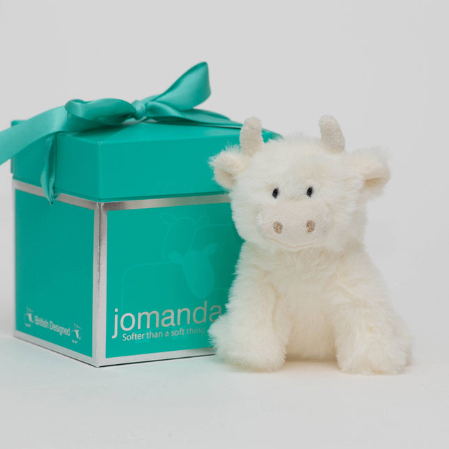 A fluffy white cow plush sits next to a teal Jomanda Soft Toys & Accessories Pop-Up Gift Box (10cm), suitable for mini toys and slippers, featuring a matching ribbon and the brandâ€™s name in white on the front.