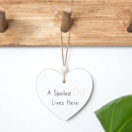 a heart shaped sign which reads a spoilt cat lives here, suspended by a piece of twine and finished with a wooden bead, hanging on a wooden coat peg