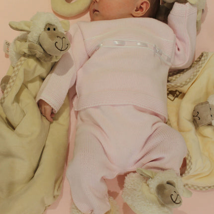 a baby surrounded by cream sheep toys including a rattle and a toy and blanket combo wearing sheep slippers