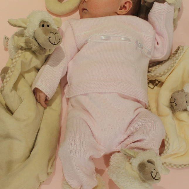 a baby surrounded by cream sheep toys including a rattle and a toy and blanket combo wearing sheep slippers