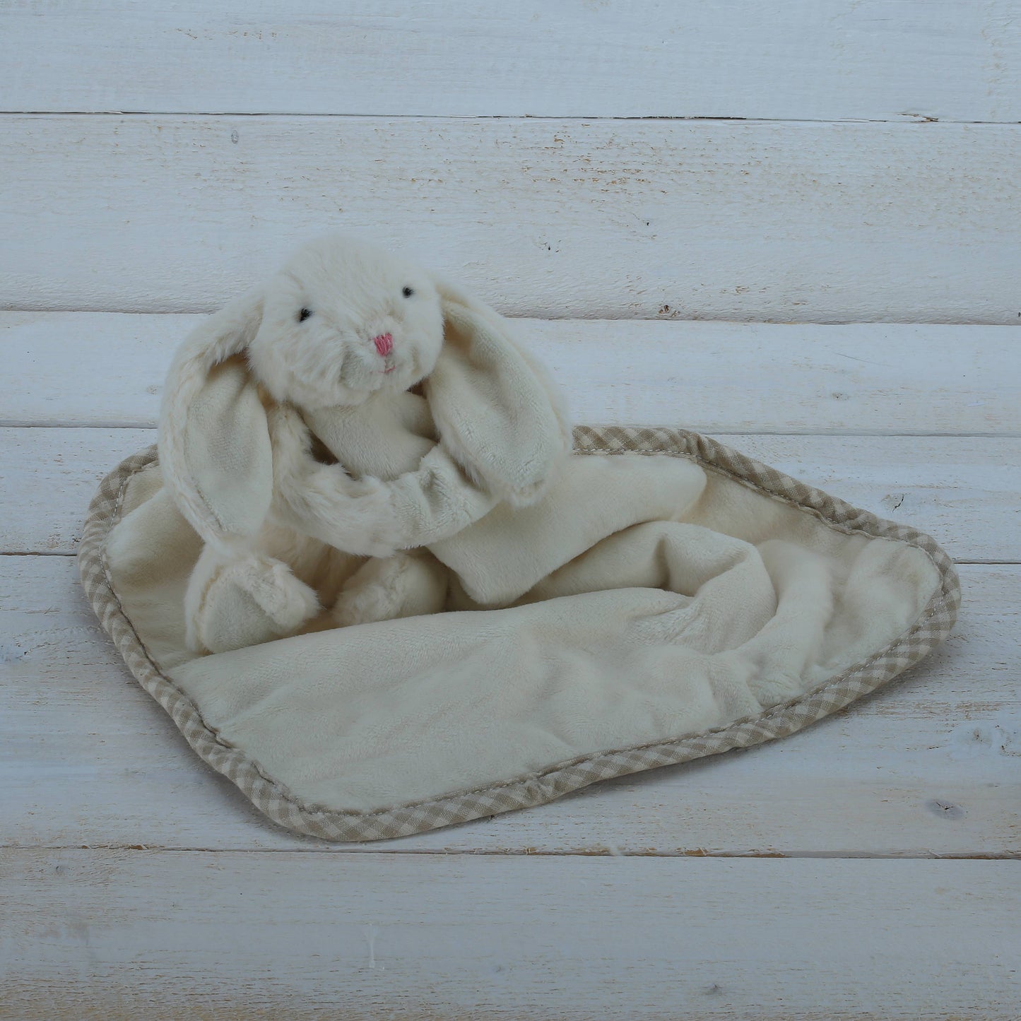 a cream fluffy bunny soft toy with floppy ears with a soft blanket comforter on whitewashed floorboards