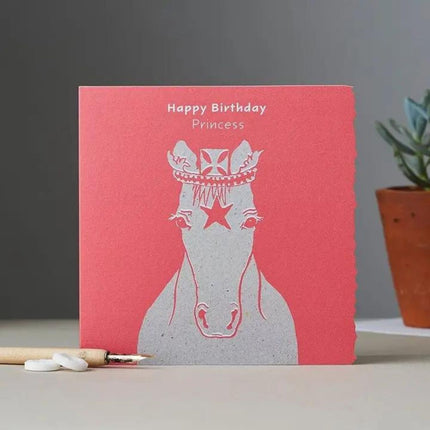 The Horse Greeting Card Happy Birthday Princess by Deckled Edge Ltd features Janna Cossettini’s simple line drawing of a crowned horse with a star, Happy Birthday Princess above, and includes pencil, eraser, and plant accents.