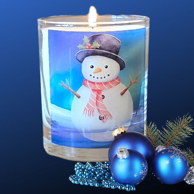 The Quaver&Lyric Christmas Scented Candle With Snowman Design On Glass Container Gift, surrounded by blue ornaments and a pine branch, creates charming festive home decor on a blue gradient background.