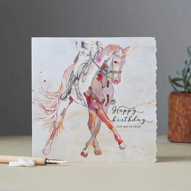The Dressage Horse Birthday Card Theme by Deckled Edge Ltd features a watercolor horse and rider with Happy birthday STEP OUT IN STYLE, plus charming paintbrush and potted plant details in the background.