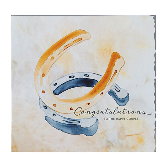 The Equestrian Wedding Anniversary Greeting Card by Deckled Edge Ltd features Janna Cossettini’s watercolor of gold and blue overlapping horseshoes and “Congratulations to the happy couple” in elegant script—ideal for horse lovers.