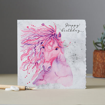 The Birthday Card For Horse Lovers Deckled Edge Pink Mare by Deckled Edge Ltd features Janna Cossettini’s artwork of a graceful pink and purple horse on a marble-like background, with “Happy Birthday” in cursive—perfect for horse enthusiasts.