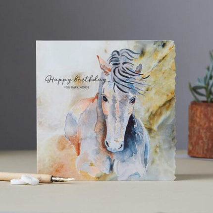 The Horse Birthday Card Dark Horse by Deckled Edge Ltd features Janna Cossettinis watercolor horse art and Happy birthday YOU DARK HORSE. Perfect for horse lovers. Pencil, erasers, and a plant shown in the background.