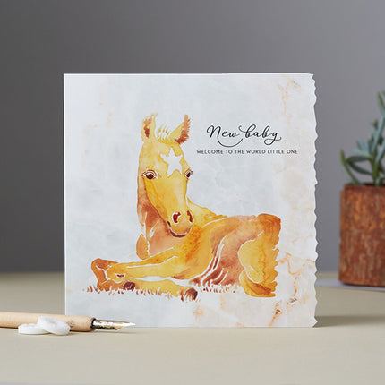 The Horse Greeting Card New Baby Welcome Deckled Edge by Deckled Edge Ltd features Janna Cossettinis watercolor chestnut foal with New baby - Welcome to the world little one on a marble-like background.
