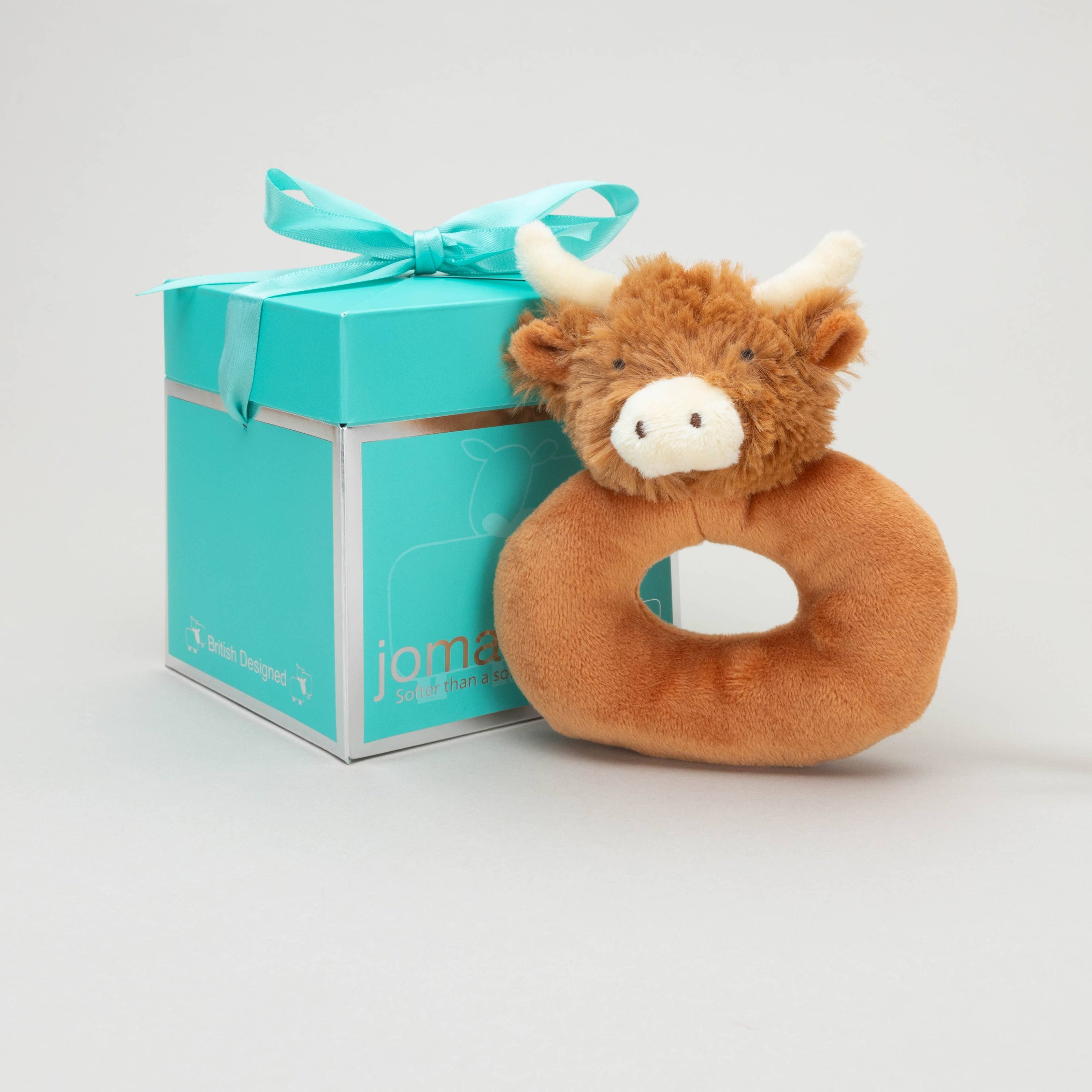 a donut shaped new baby rattle in brown soft plush fabric with a cute brown highland cows head with cream horns and ears next to a jomanda branded gift box