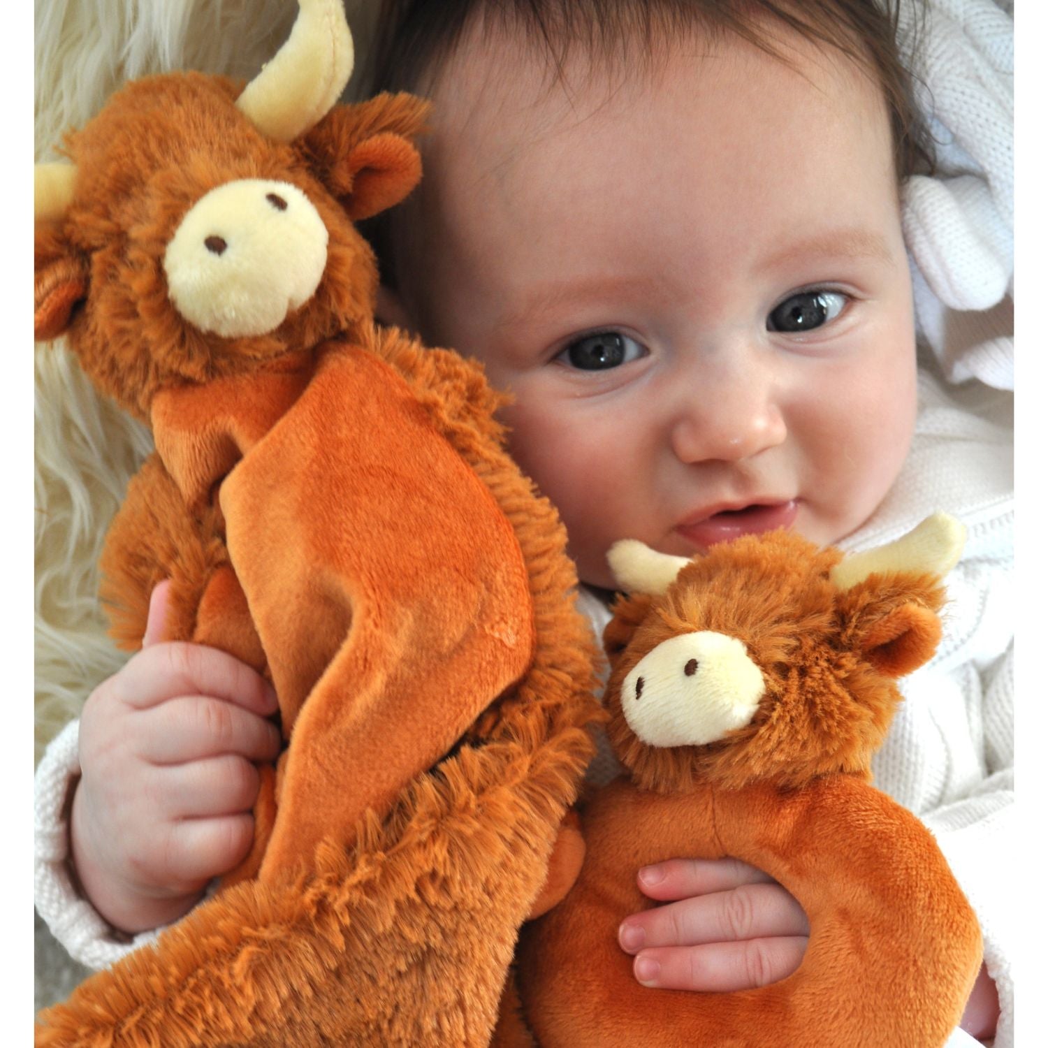 a baby snuggling up to the highland cow soother and holding the highland cow rattle