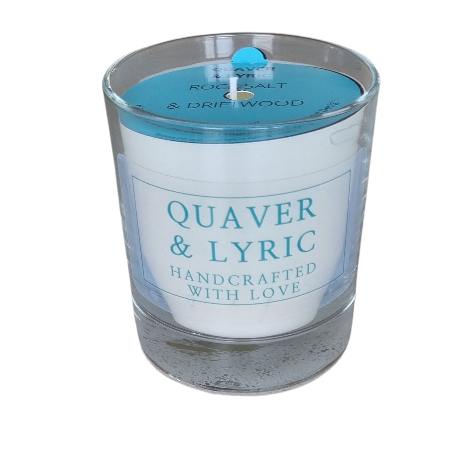 a candle in a glass with quaver & lyric handcrafted with love label and blue dust cover