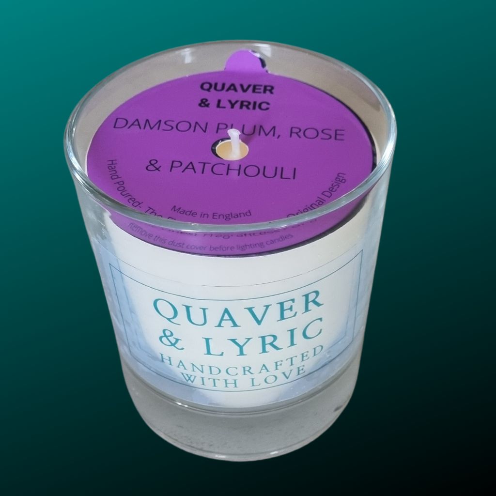 a candle in a glass with quaver & lyric handcrafted with love label and pink dust cover on a teal background