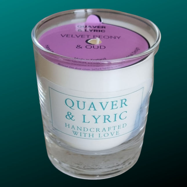 a candle in a glass with quaver & lyric handcrafted with love label and pink dust cover on a teal background