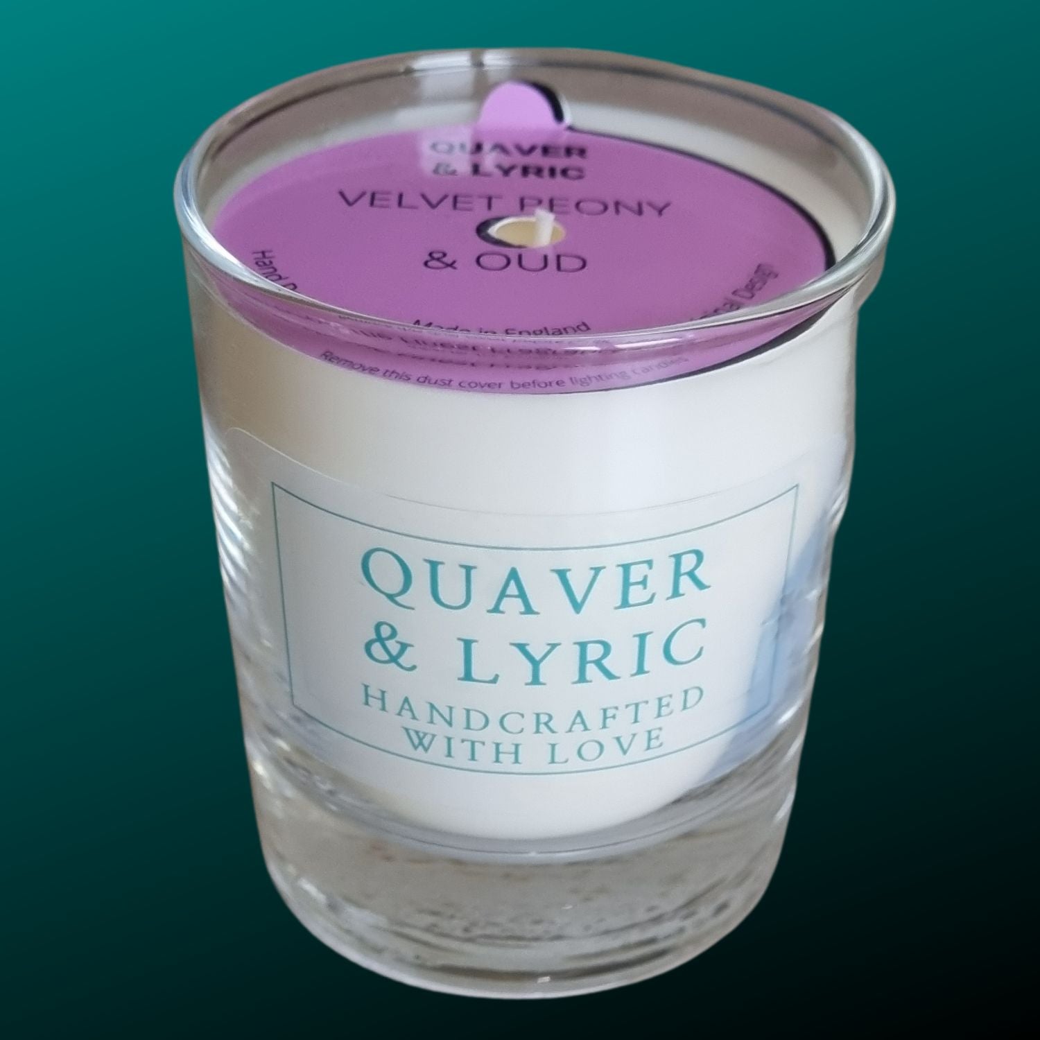 a candle in a glass with quaver & lyric handcrafted with love label and pink dust cover on a teal background