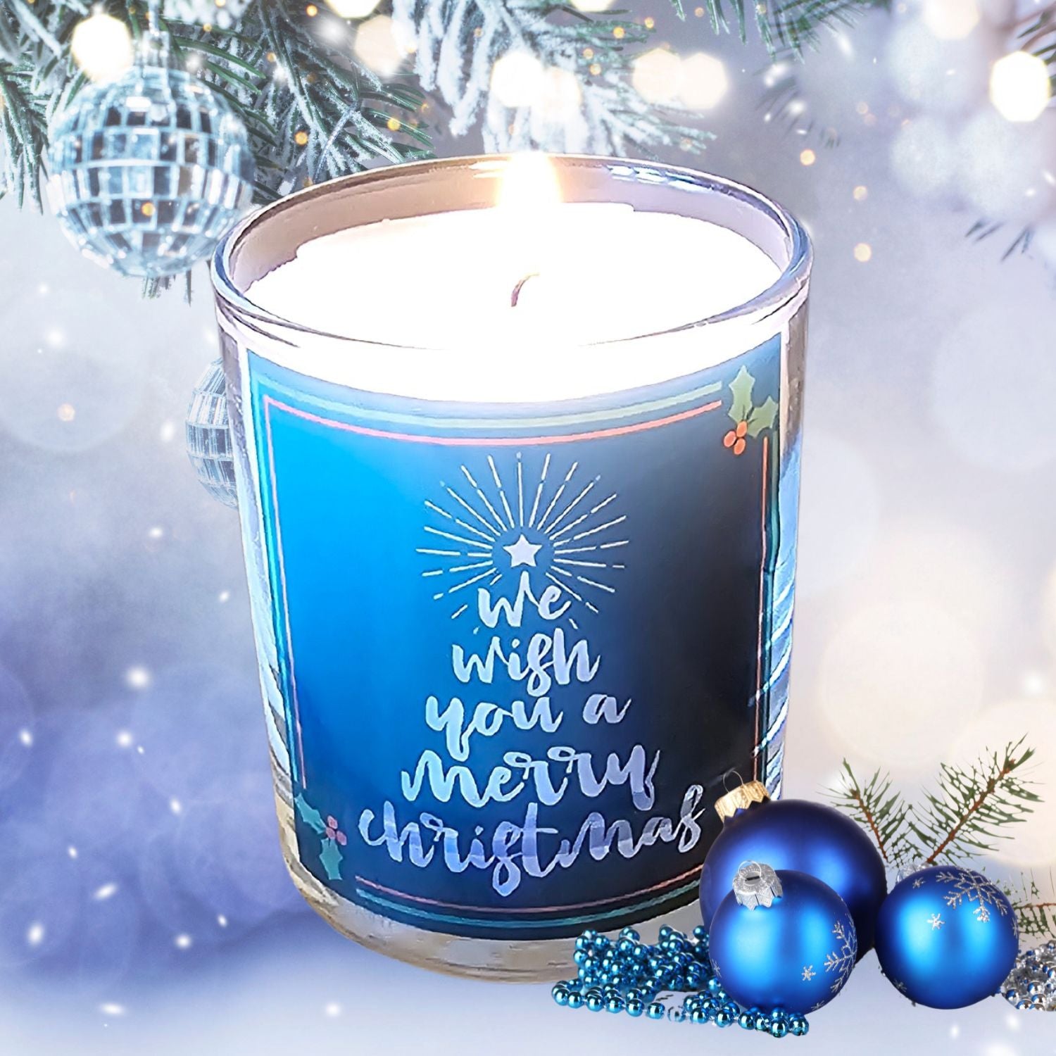 The Quaver&Lyric Christmas Scented Candle “Wish You A Merry Christmas” Glass Container Gift is shown lit, surrounded by blue ornaments and beads, with pine branches and silver decor on a snowy background.