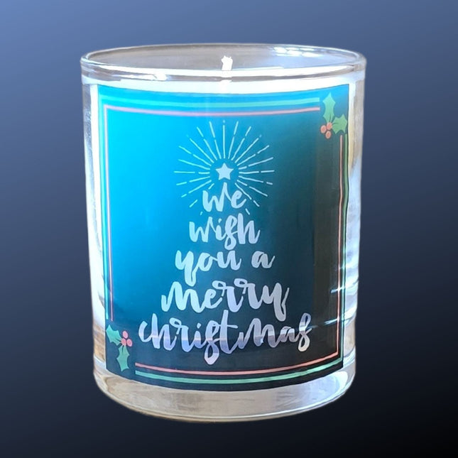 The Quaver&Lyric Christmas Scented Candle comes in a glass container with Wish You A Merry Christmas and holly on a blue background, topped by a tree—perfect festive decor or gift for the holiday season.