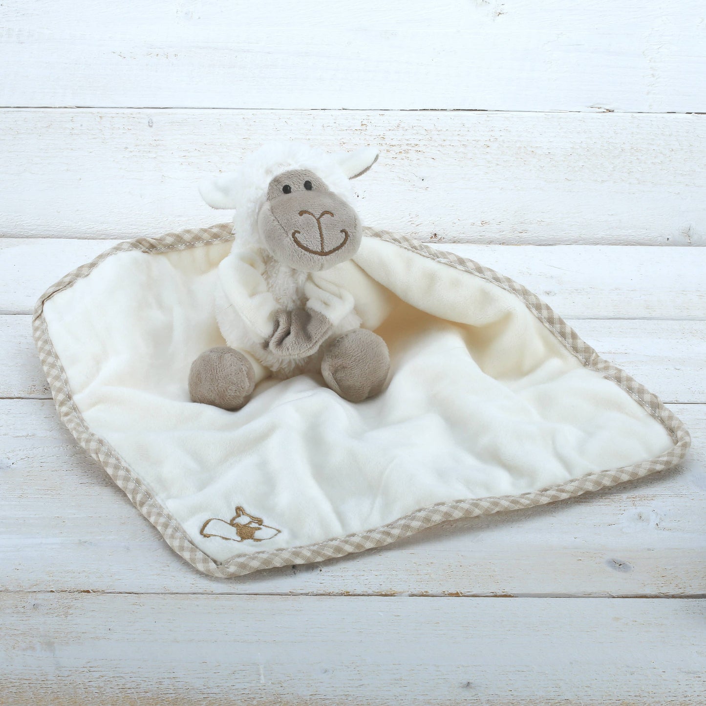 an adorable cream plush sheep soft toy with beige embroidered face on a cream comforter blanket