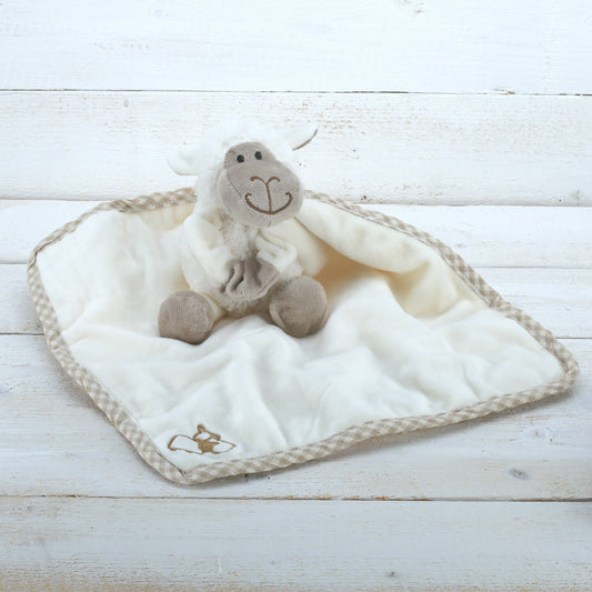 an adorable cream plush sheep soft toy with beige embroidered face on a cream comforter blanket