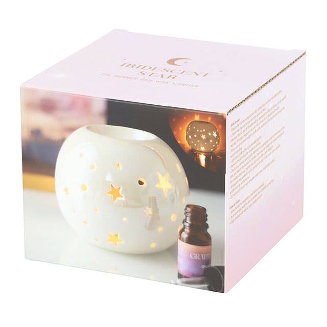 the packaging of the oil burner showing the wax warmer with stars cut out and and irridescent finish next to a bottle of fragrance oil on the front