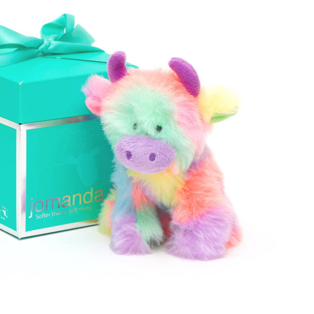 A 10cm rainbow-furred highland cow plush with purple horns by Jomanda Soft Toys & Accessories sits beside a Jomanda-branded Gift Box Pop-Up, finished with a turquoise ribbonâ€”perfect for mini toys or slippers.