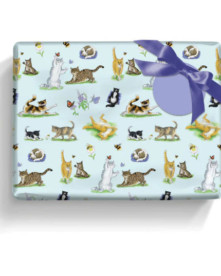 a gft wrapped in paper featuring a variety of adorable cats with flowers, bees and butterflies on a pale blue background with a round lilac gift label