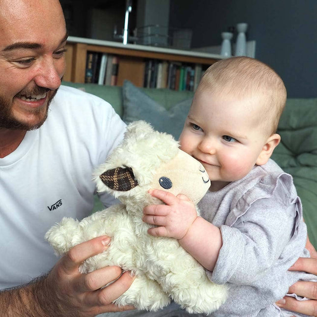 A smiling man and a baby enjoy the Pull Along Toy Sheep Lambert by Little Bird Told Me UK, sitting together on a sofa in a cozy living room, encouraging tactile stimulation and development.