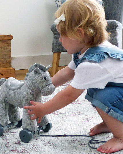 a baby girl playing with an an adorable grey cuddly pony made from herringbone fabric on detachable wheels with textured mane and tail