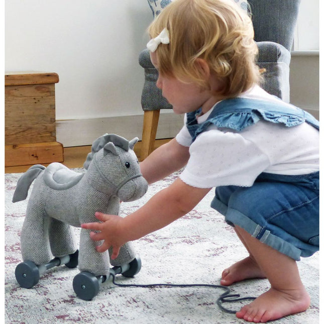 a baby girl playing with an an adorable grey cuddly pony made from herringbone fabric on detachable wheels with textured mane and tail