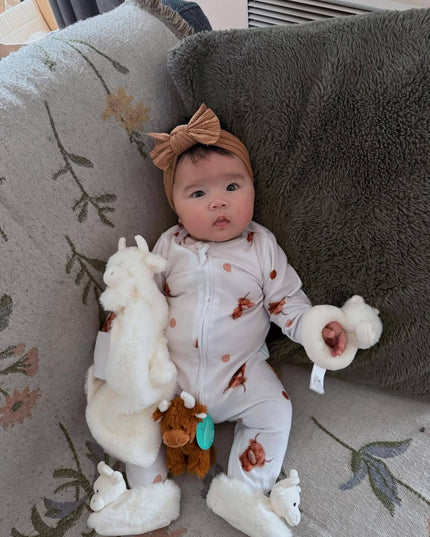 a baby with the highand cow rattle and soother wearing a pair of fluffy cream highland cow baby boots from Jomanda toys