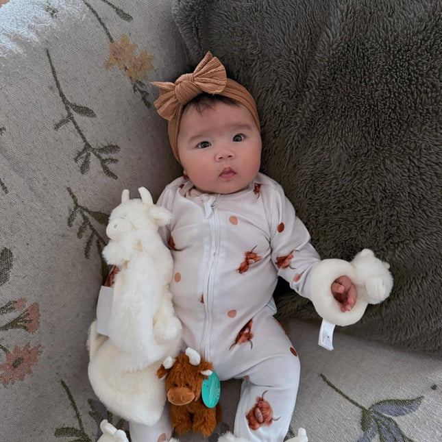 a baby with the highand cow rattle and soother wearing a pair of fluffy cream highland cow baby boots from Jomanda toys