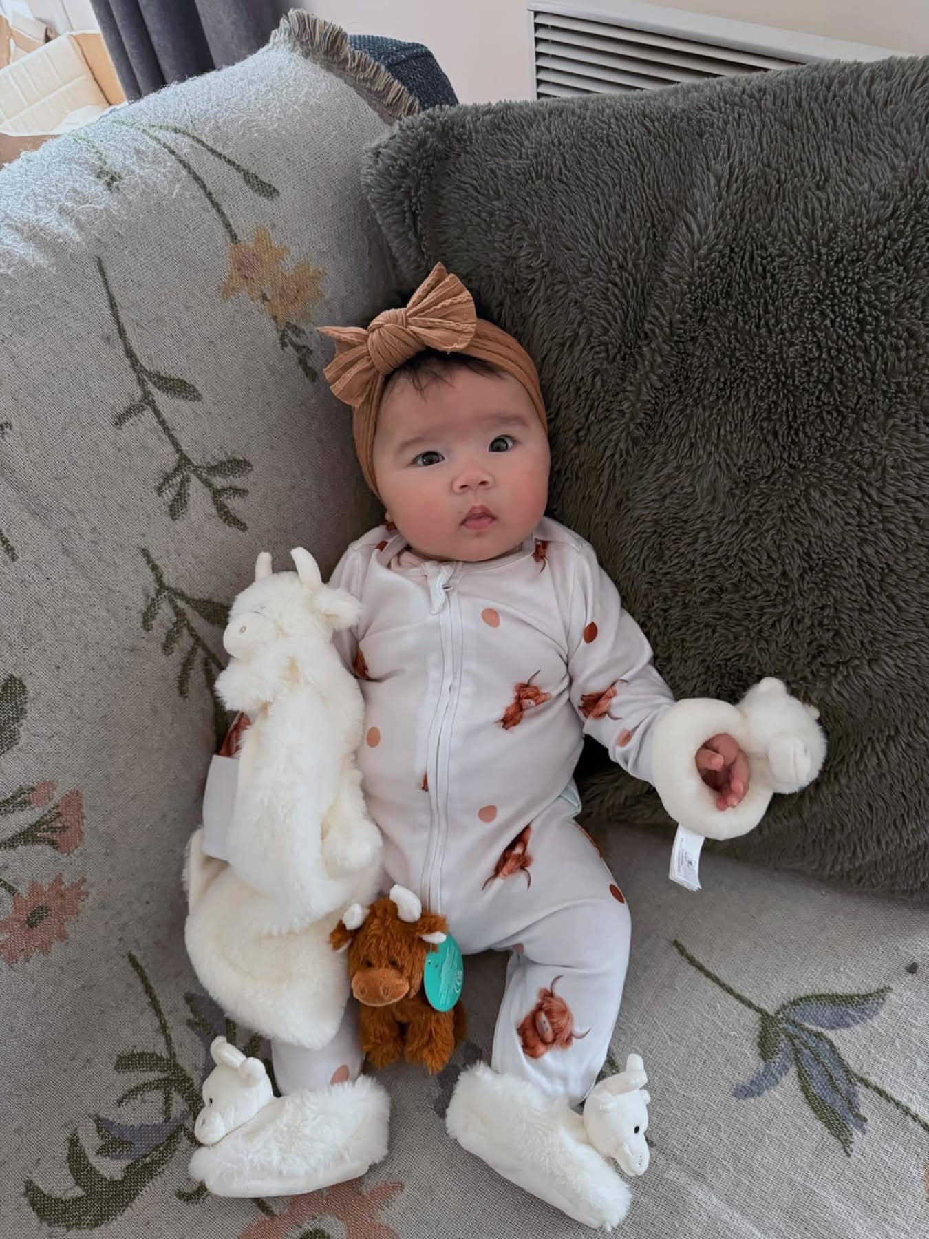 a baby with the highand cow rattle and soother wearing a pair of fluffy cream highland cow baby boots from Jomanda toys