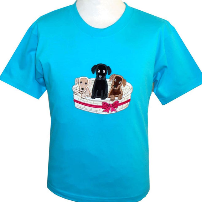 The British Country Collectionâ€™s Dog T Shirt features an embroidered basket of three puppiesâ€”beige, black, and brownâ€”sitting together. This childrenâ€™s tee is bright blue and perfect for young dog lovers.