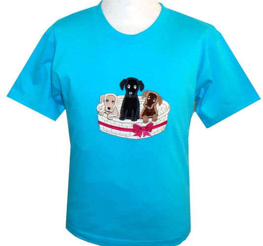 The British Country Collection’s Dog T Shirt features an embroidered basket of three puppies—beige, black, and brown—sitting together. This children’s tee is bright blue and perfect for young dog lovers.