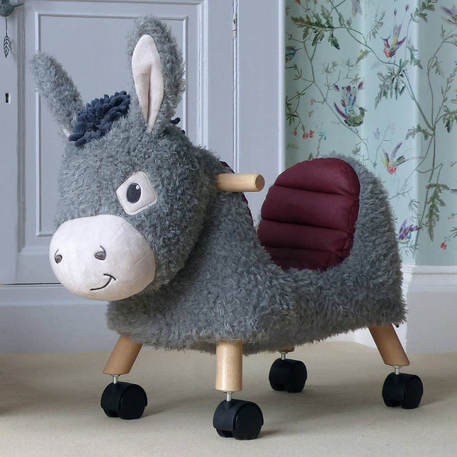 an adorable donkey ride on toy with a cute smiling face and deep curved seat on a wooden frame with castors in a room setting