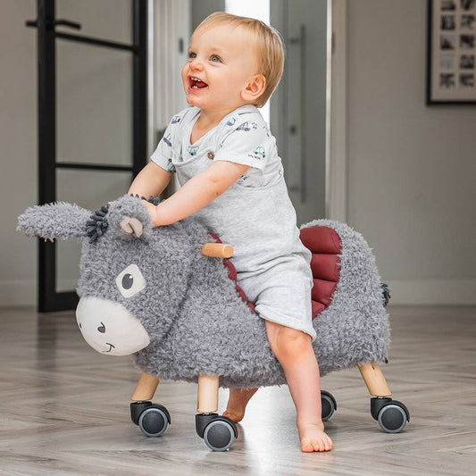 a happy baby riding on an adorable donkey ride on toy 