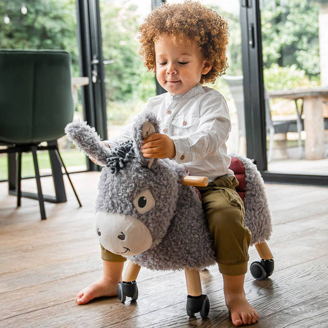 a toddler riding on an adorable donkey ride on toy and playing with the donkey's textured ears