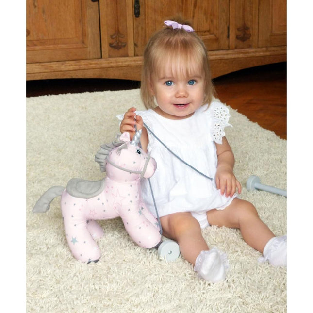 a baby girl playing with a pink unicorn pull aong toy on wheels.