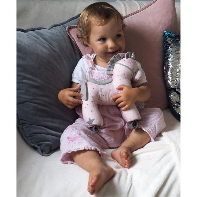 a baby girl playing with a pink cuddly unicorn toy.