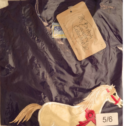 A folded purple kids’ T-shirt by British Country Collection, size 5/6, in plastic packaging features an embroidered cream horse with a red ribbon and “Champion Pony” applique design.