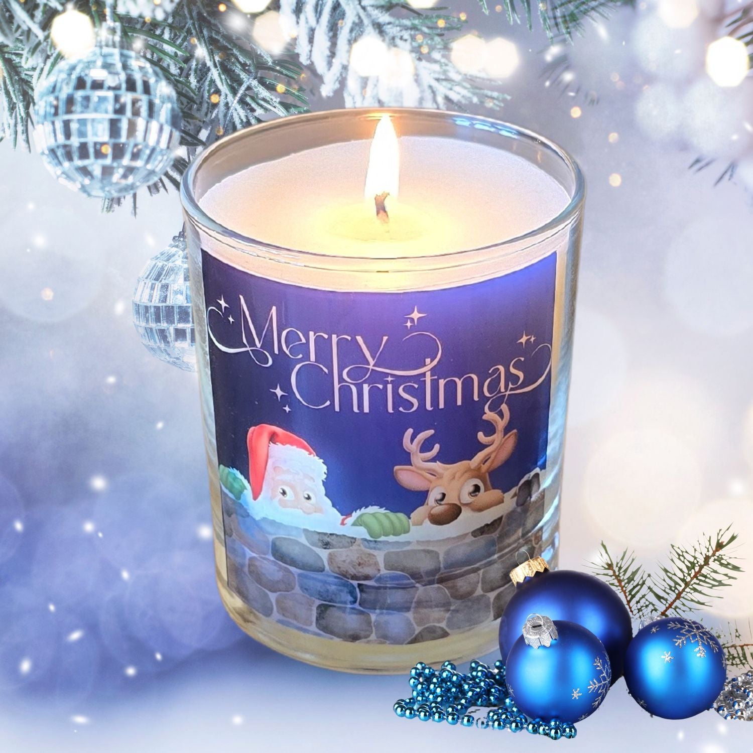 A lit Christmas scented candles with a charming Merry Christmas design featuring Father Christmas and a reindeer peeping over a wall. The candle is set in a snowy festive setting.