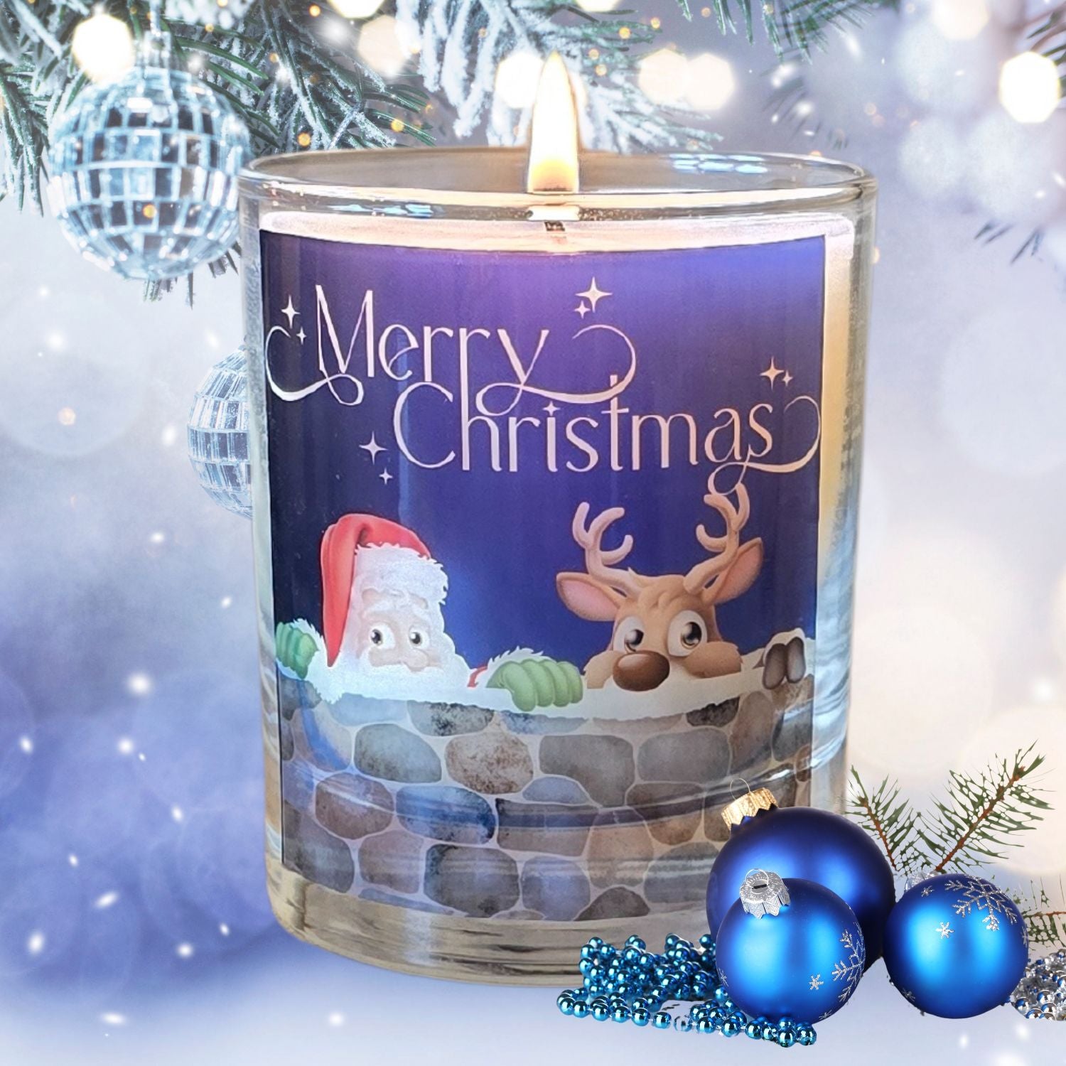 A lit Christmas scented candles with a charming Merry Christmas design featuring Father Christmas and a reindeer peeping over a wall. The candle is set in a snowy festive setting.