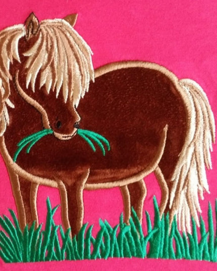 The British Country Collections Horse T Shirt features an embroidered Shetland pony with a blond mane on green grass against a bright pink backgroundâ€”a charming pick for horse lovers.