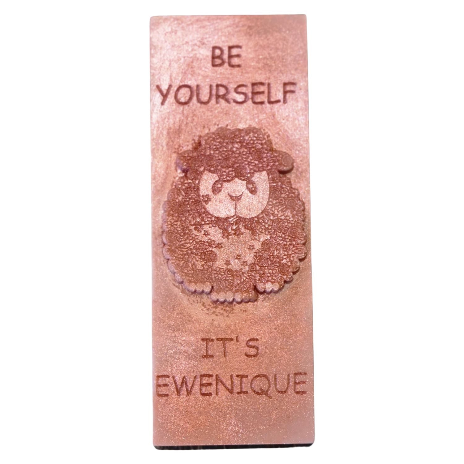 A bronze coloured rectangle of wax with a raised sheep design with the writing be yourself above and it's ewenique below.
